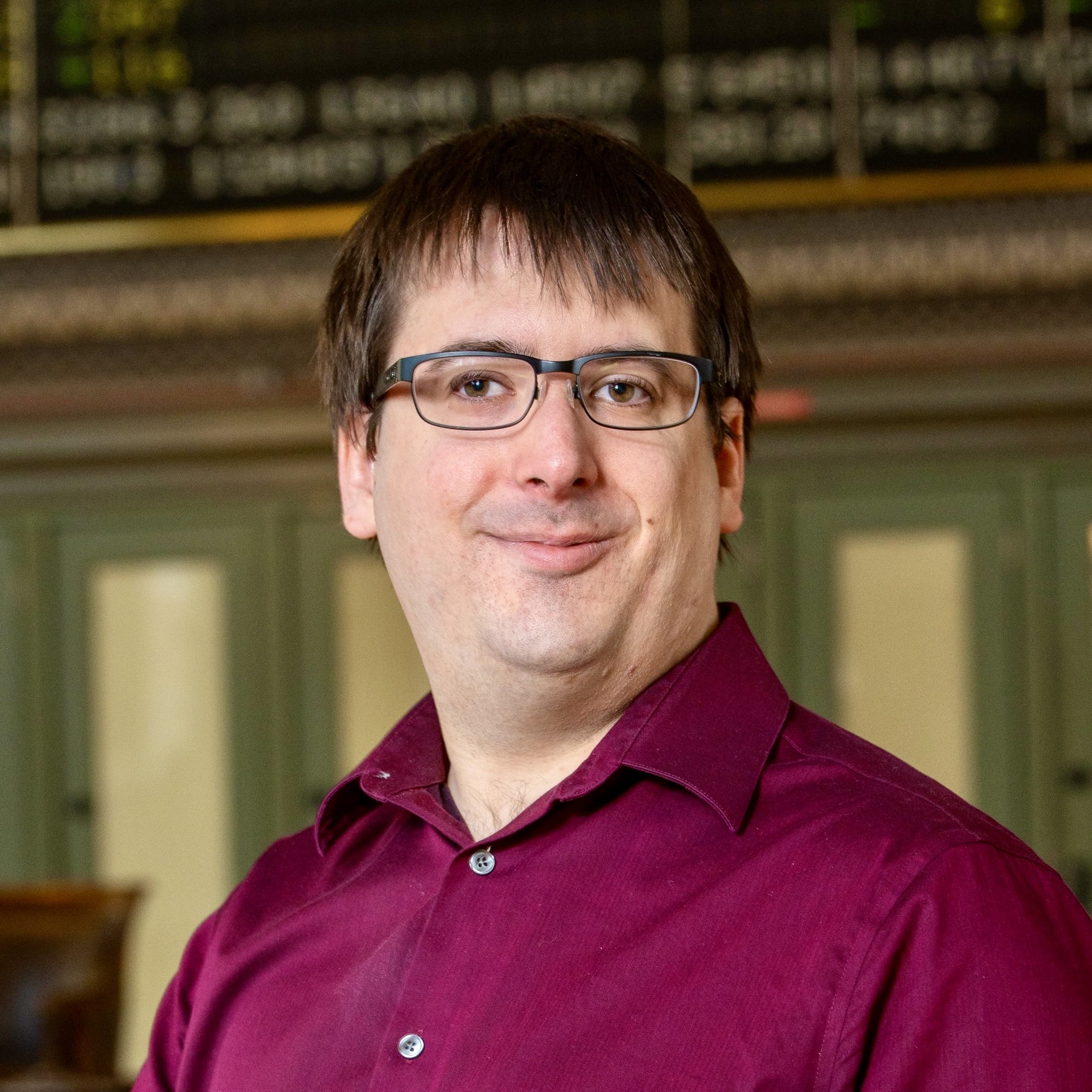 Professional head shot of Nick Zelany wearing a maroon  button down shirt and black glasses